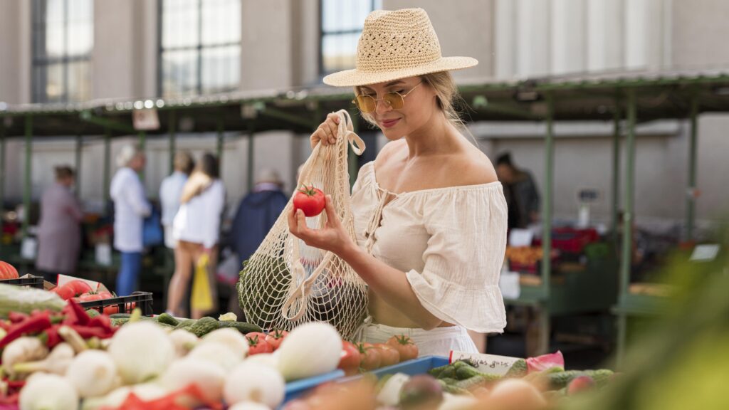 Woman in Larnaca, Cyprus market selecting tomatoes, with a full mesh bag of fresh produce.