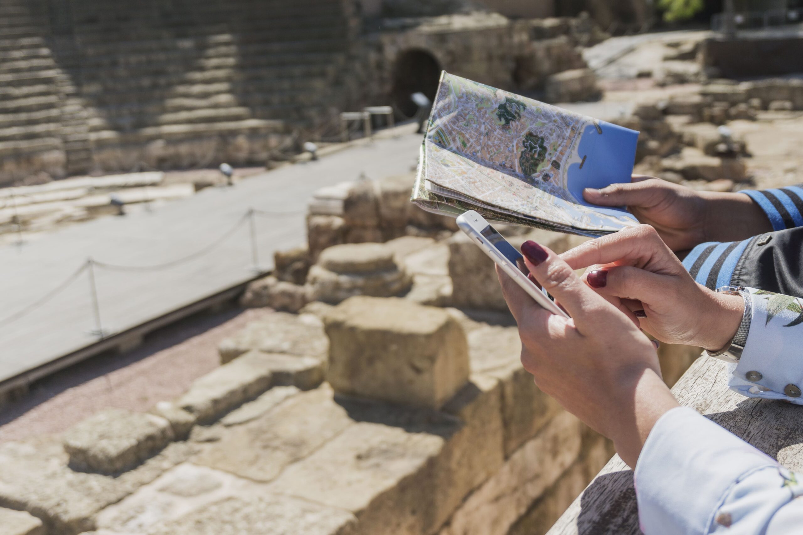 Two people using a map and smartphone for navigation at an ancient amphitheater in Cyprus