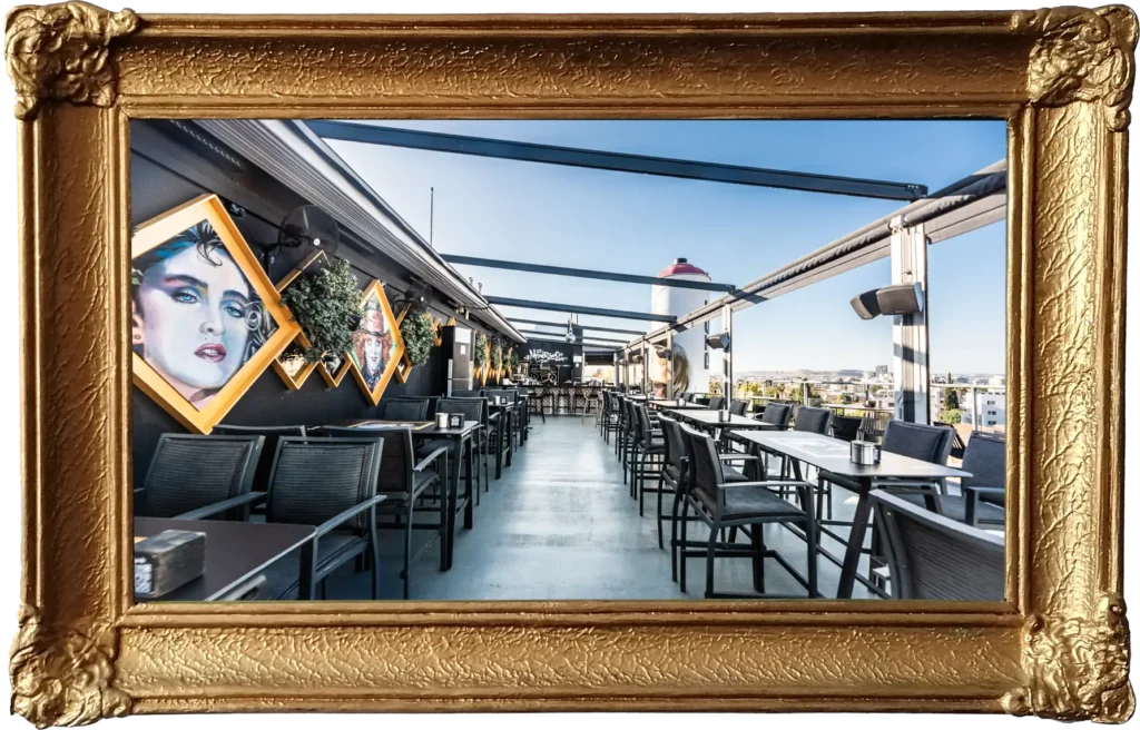 Memories rooftop seating area with tables and chairs, featuring wall art of famous faces and a large spray paint can decoration in the background under a clear blue sky.