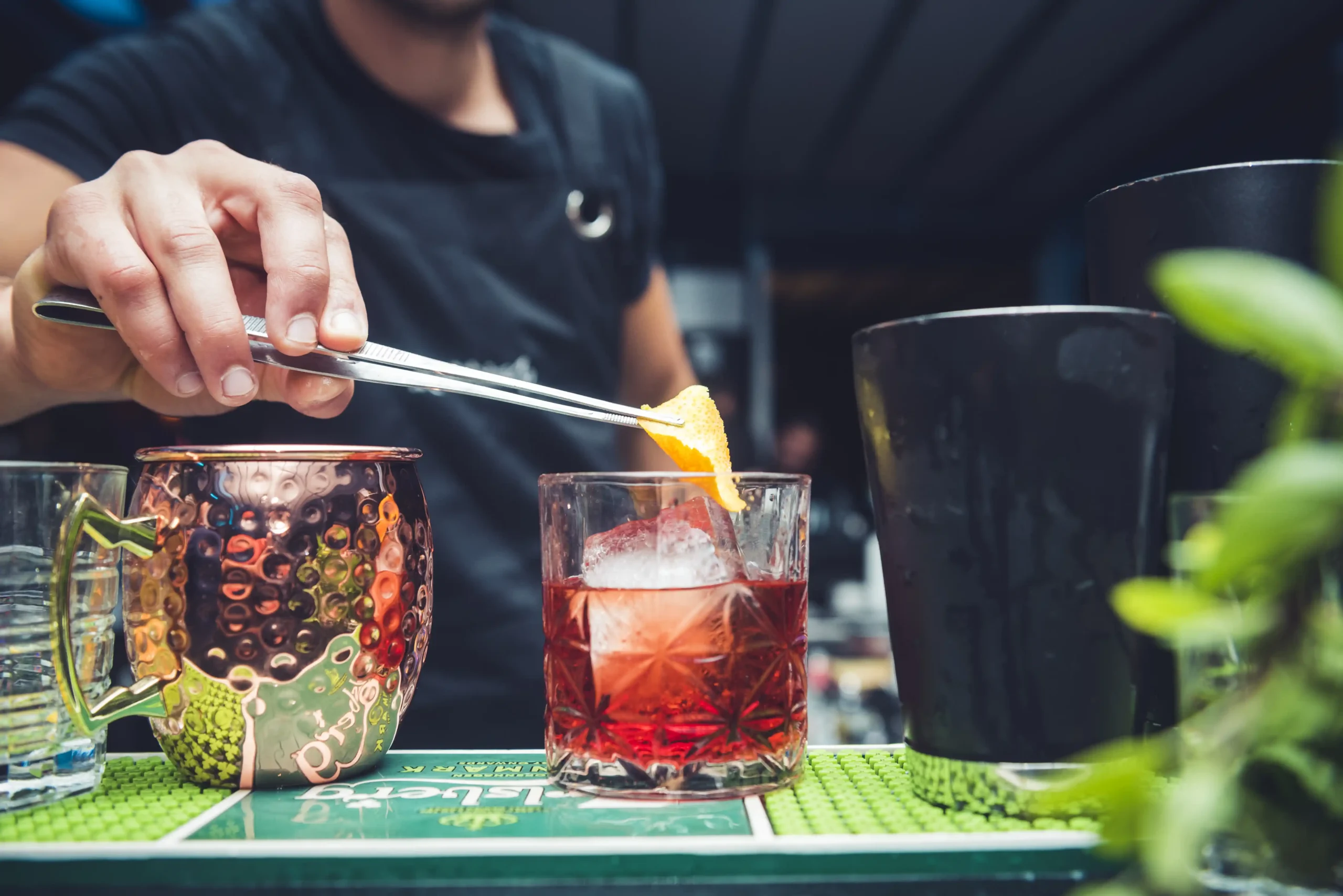 A bartender adding a citrus twist to a Negroni Cocktail with various cocktail glasses in the foreground.
