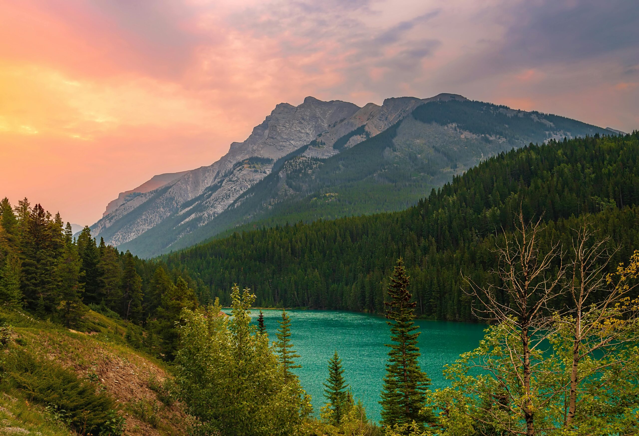 Stunning mountain landscape with a turquoise lake and dense forest under a vibrant sunset sky in Cyprus.