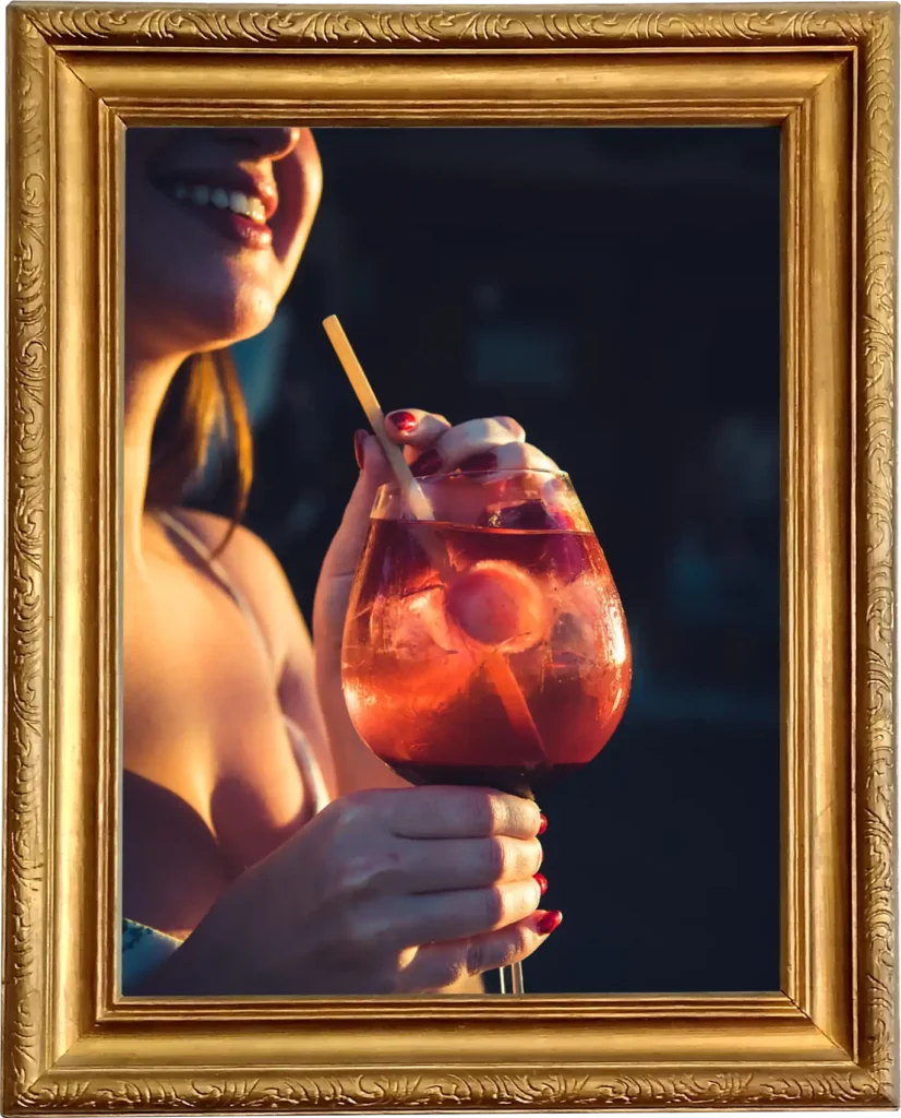 A woman holding a pink cocktail and smiling during sunset.