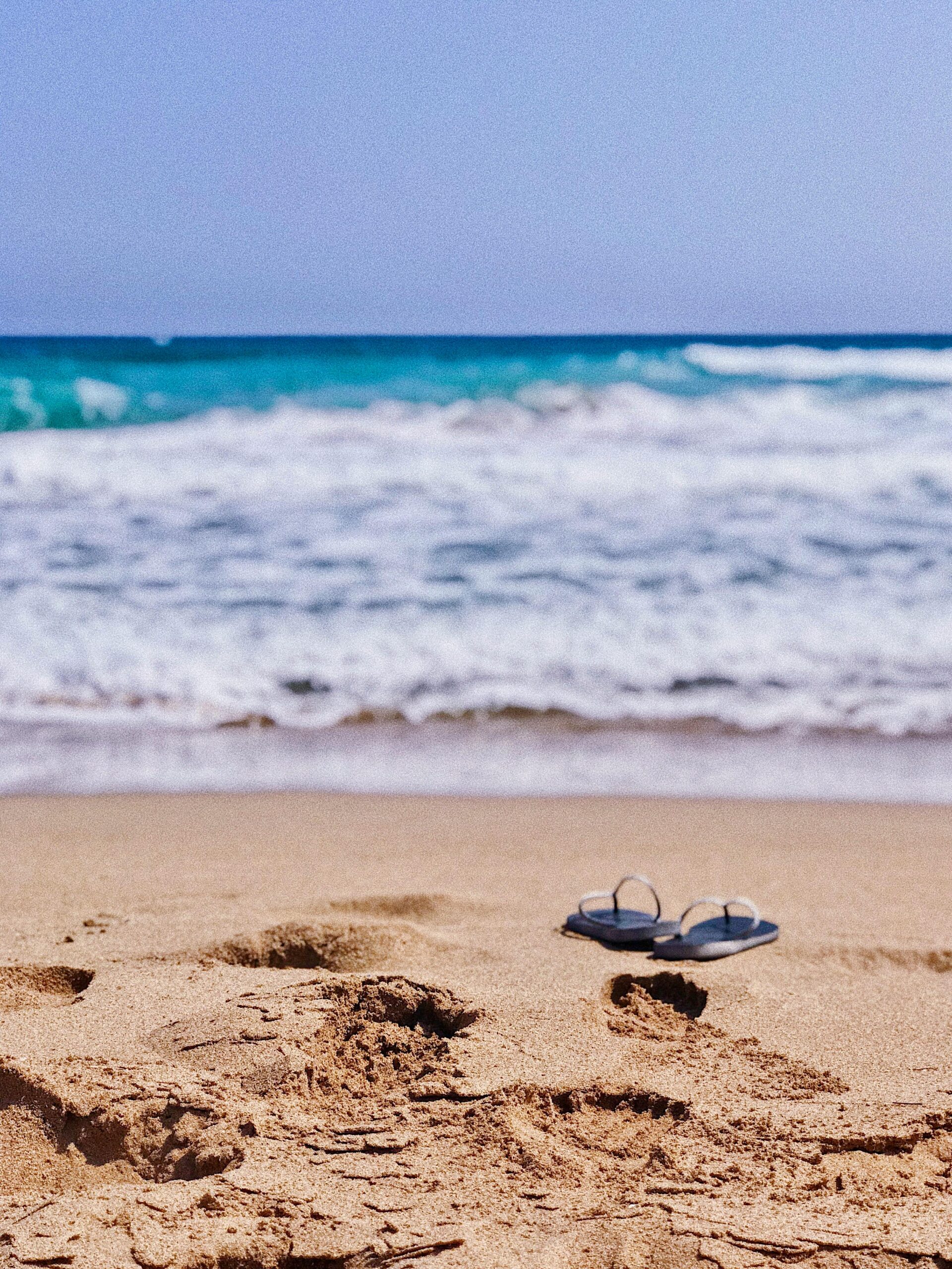 Flip-flops on a sandy beach with ocean waves in the background in Cyprus