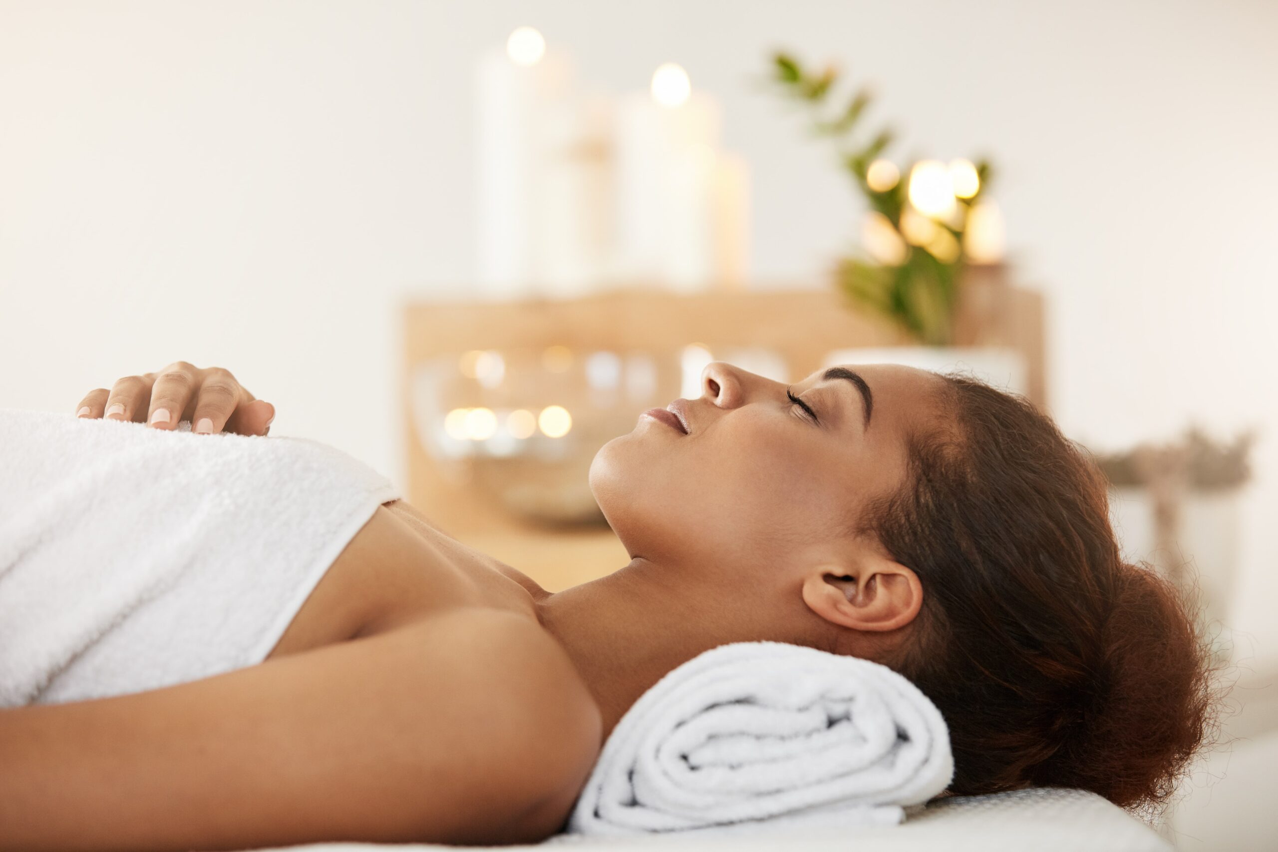 Woman relaxing at a spa, wrapped in a towel with calming candles in the background.