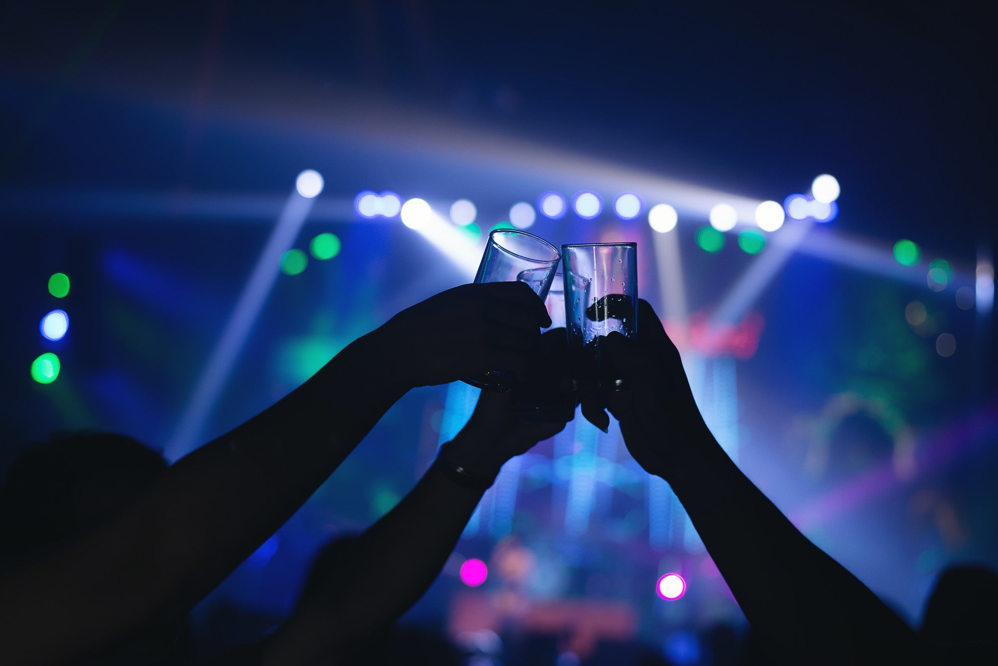 Silhouettes of people clinking glasses at a vibrant nightclub with colorful lights in the background.